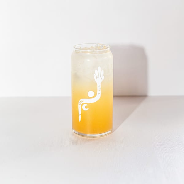 A glass of Stoke Salad's orange beverage with ice and a white logo on a white background.