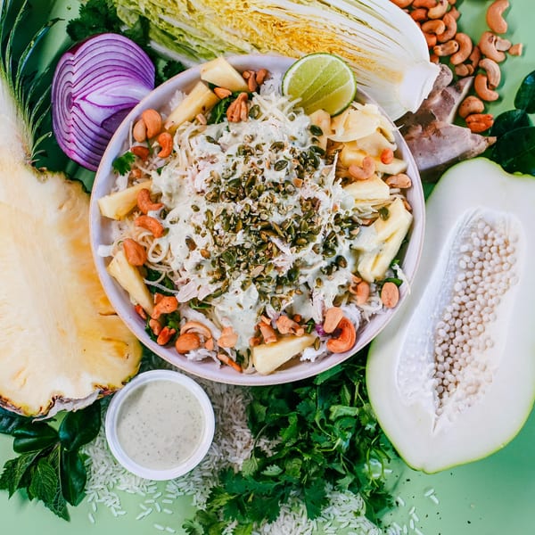 Stoke Salad's vegetarian bowl with pineapple, cashews, and dressing, surrounded by fresh ingredients.