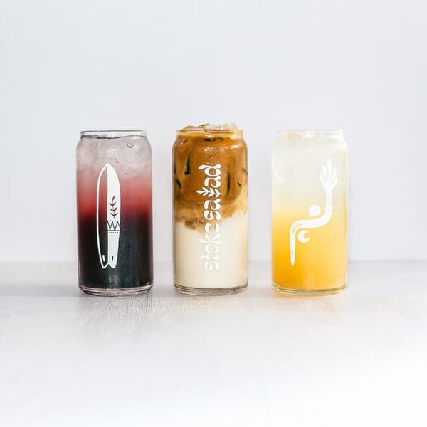 Three tall glasses of colorful iced drinks, including a layered coffee and two fruit beverages.