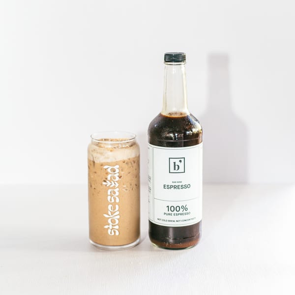 A glass of iced coffee with "Stoke Salad" branding next to a bottle of Bar Nine espresso.